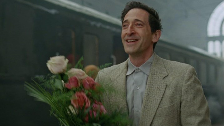 A man holds a bouqet of flowers in The Brutalist.