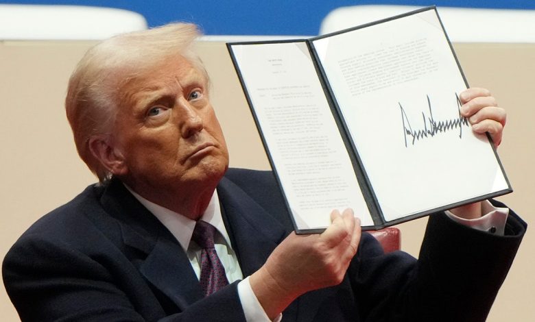 President Donald Trump holds up an executive orders after signing it