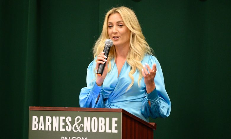 Liana Werner-Gray speaking at a dais. She is wearing a blue top and she is holding a microphone.