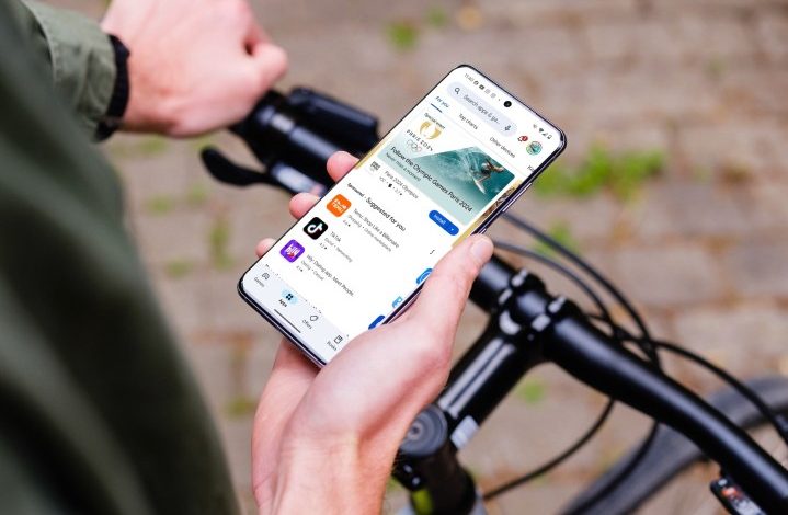 A person holding an Android phone while on a bike. The display shows the Google Play Store.