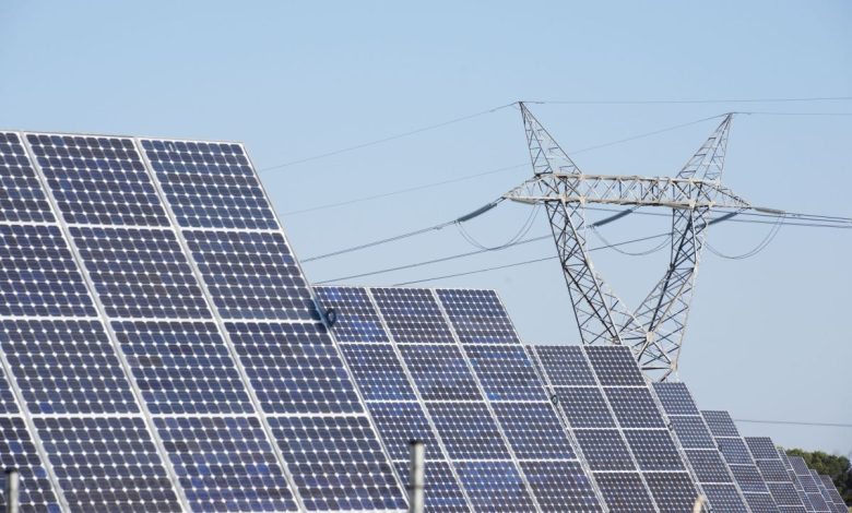 Solar panels stand in front of a high-voltage power line.