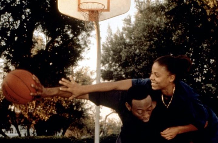 A guy holds a ball away from a girl on the basketball court.