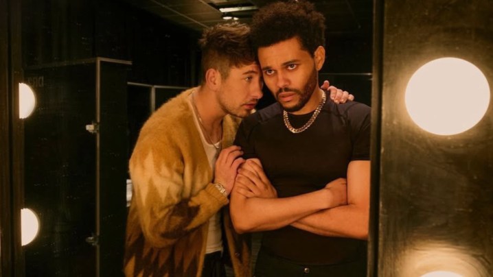 Barry Keoghan talks into The Weeknd's ear as they stare into a mirror.