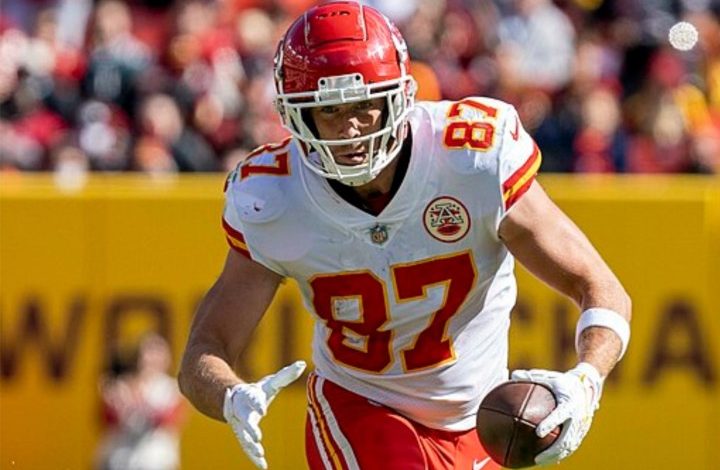 Travis Kelce holds the ball with one hand and runs.