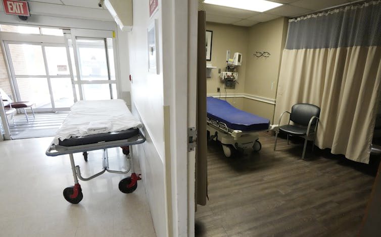 Two empty hospital beds in a room and a hallway near the entrance