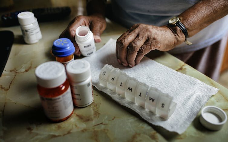 Person sorting through pills, a variety of pill bottles and a weekly pill box beside them