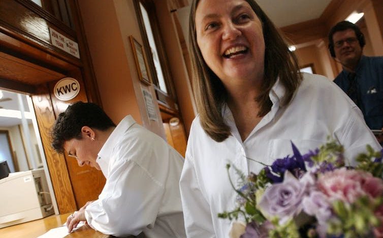 A woman fills out a marriage license as her partner holds a bouquet.