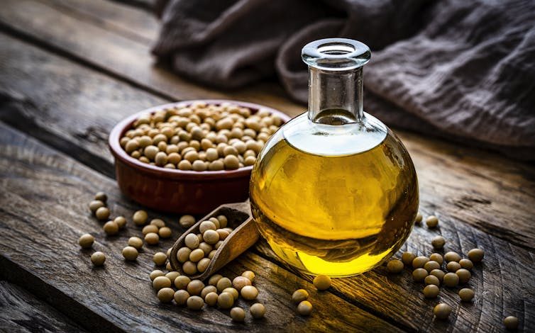 A small bottle of soybean oil beside a bowl of soybeans, on a wooden table