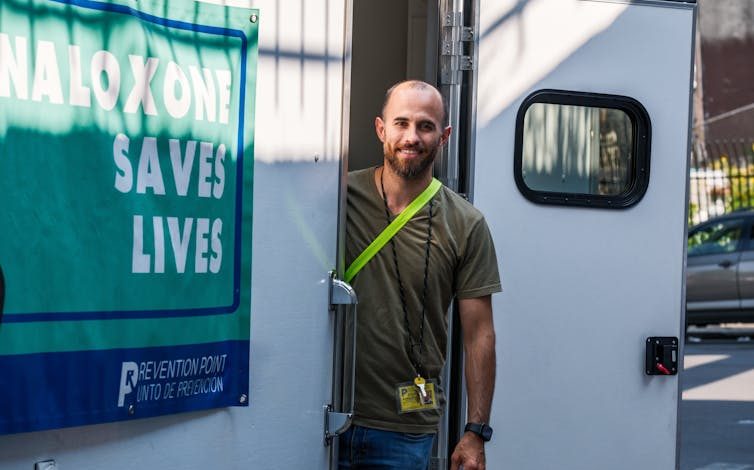 Man stands on steps of white van with sign on its outside that says Naloxone Saves Lives