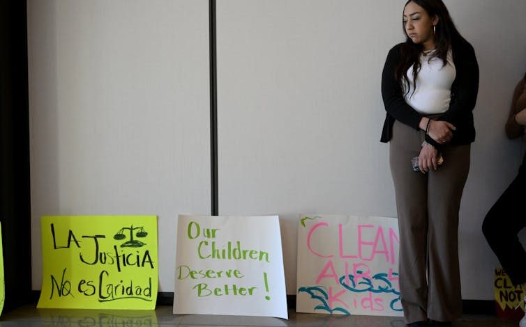 A woman stands in front of posters that call for air pollution justice and