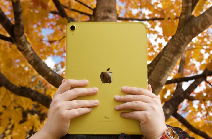 Someone holding the yellow iPad (2022) in front of trees with orange, yellow leaves.