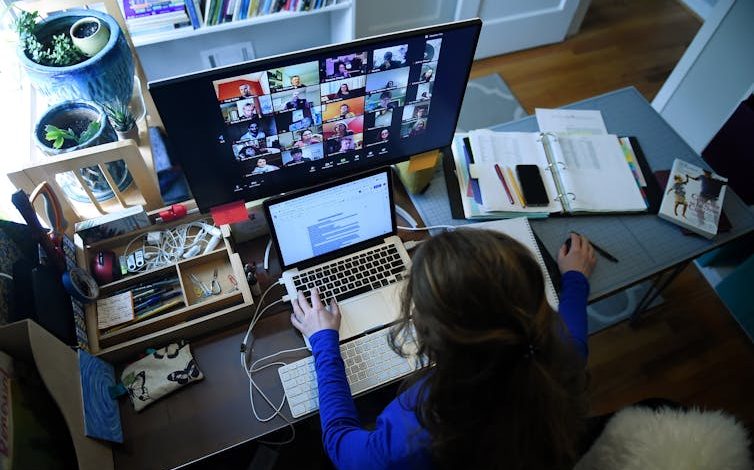 A teacher sits at home in front of a computer monitor.