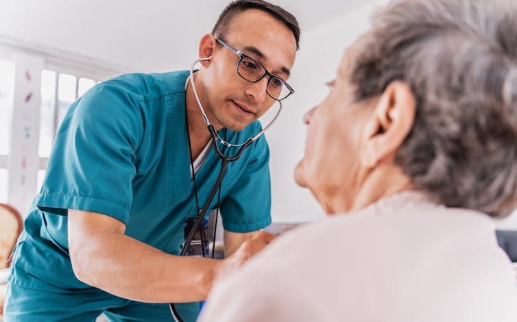 Nurse listening to heartbeat of a senior woman during medical consultation