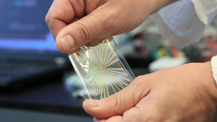 Close-up of a person's hand stretching a gel-like material with an array of metal strips radiating from the center towards the edges