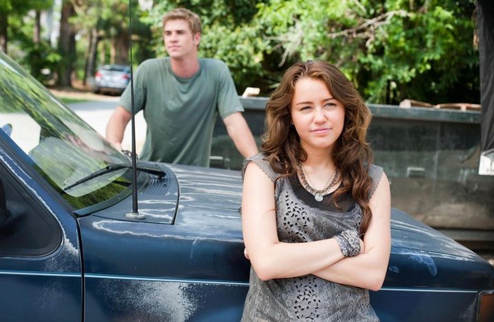 Miley Cyrus stands in front of a car.