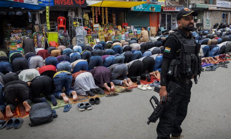 Kashmiri Muslims offering Friday prayers while Indian security guard stands watch