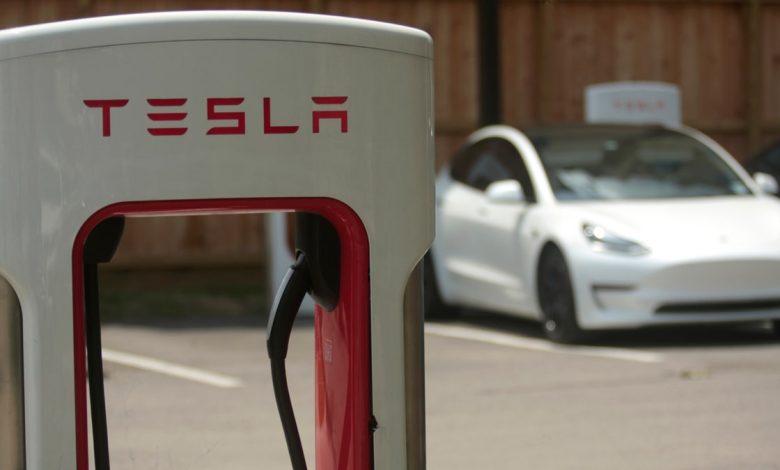 A Tesla supercharging location is seen with a white Tesla in the background.
