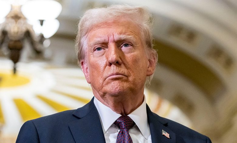 Donald Trump in a navy jacket and purple tie looks to his right