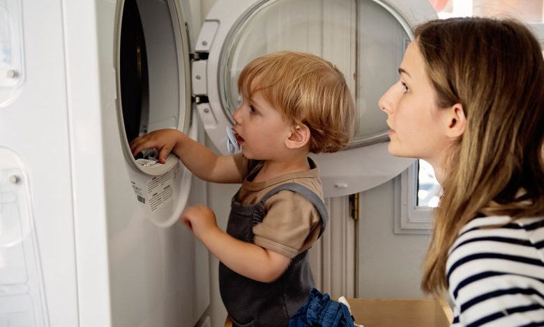 Child and mother looking into a washing machine from the side.