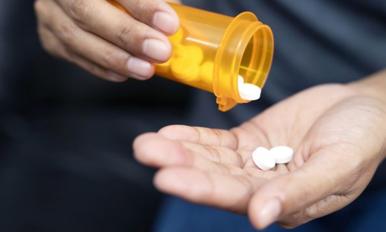 Woman hand with pills on, spilling pills out of bottle on dark background.