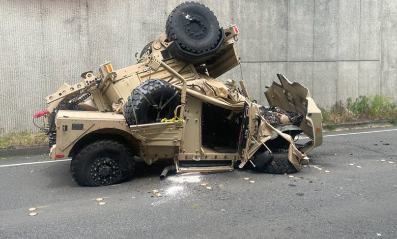 Wrecked military Humvee and trailer on a city street below an overpass