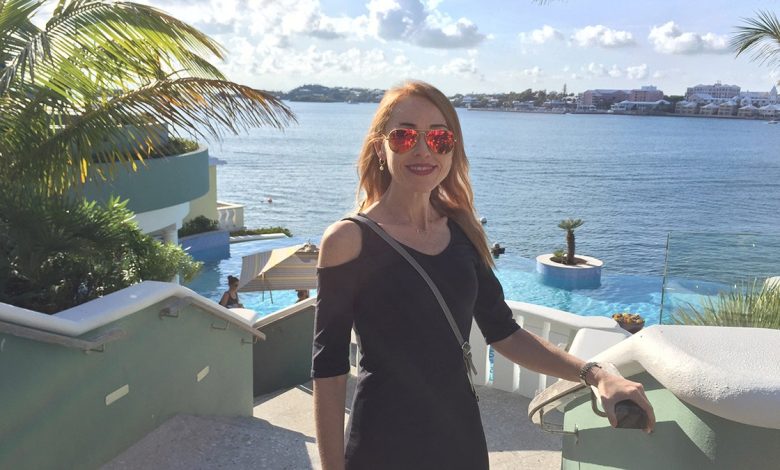 Terrilyn Griffith standing in front of an ocean view. The blonde woman has sunglasses on and she is smiling. Pre-injury.