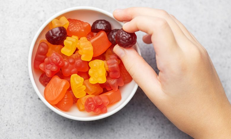 hand holds a gummy vitamin over a bowl