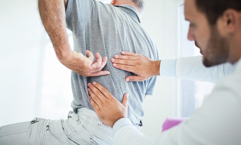 Spinal surgeon feels patient's back as he gestures to specific area.