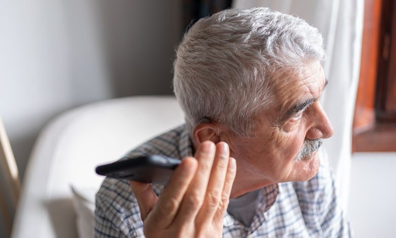 Senior Man With Hearing Aid Using Smartphone