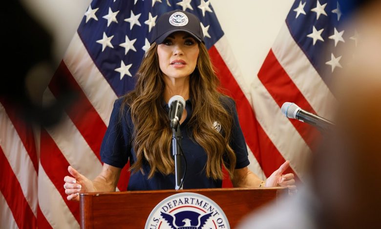 Homeland Security Secretary Kristi Noem speaking at a podium wearing a blue DHS hat