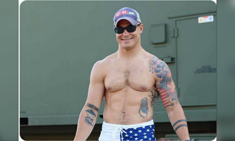 Travis Decker pictured with a clean shave and shirtless, showing tattoos on both arms and his left side