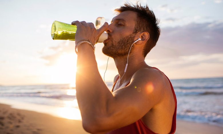 man drinks from bottle on the beach during a workout