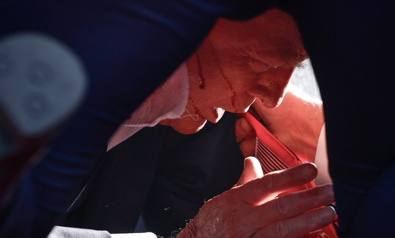 Donald Trump lies down on the ground with a drip of blood running down his cheek